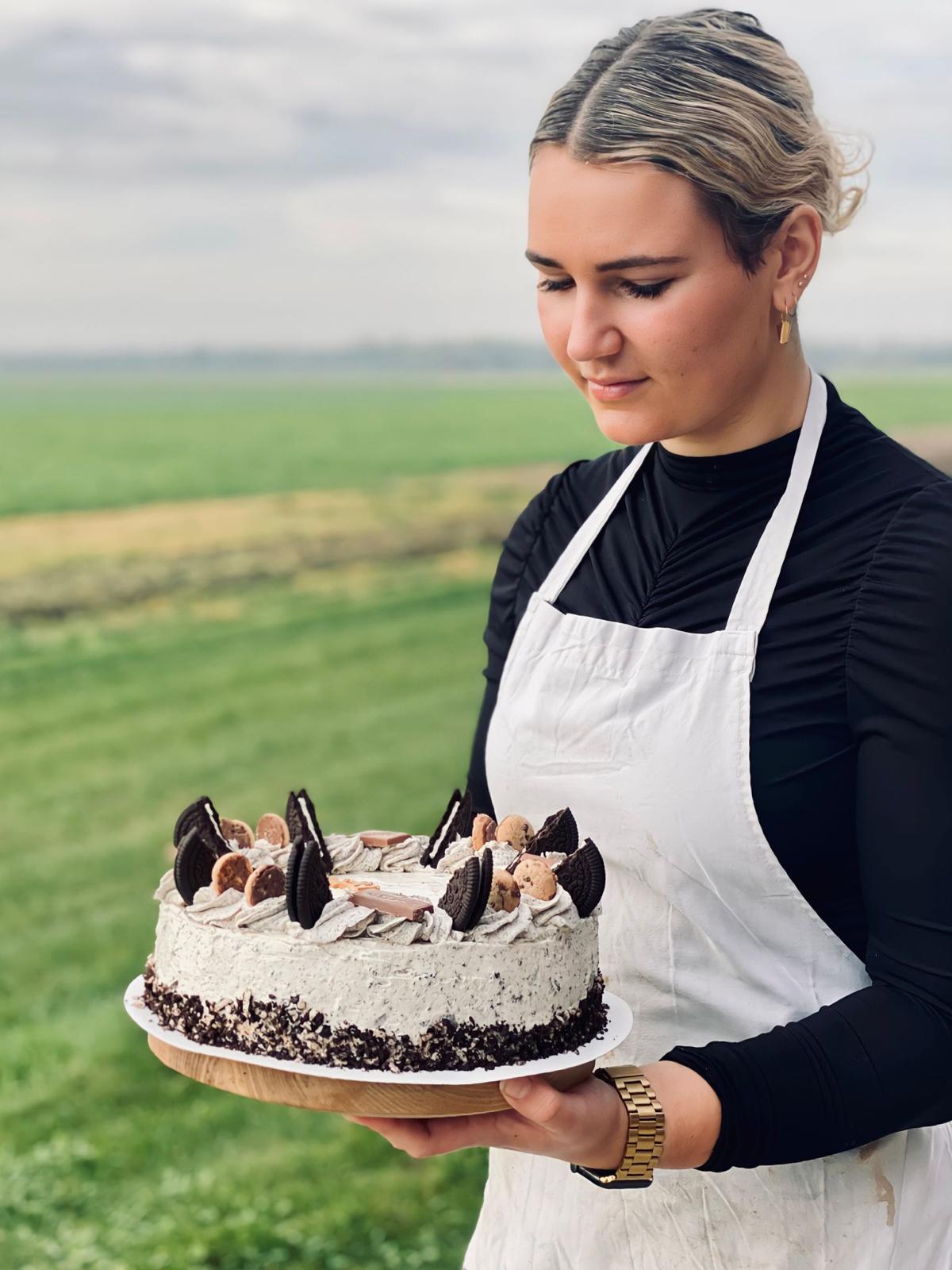 Vrouw met zelfgemaakte hoge taart in handen, buiten weids uitzicht
